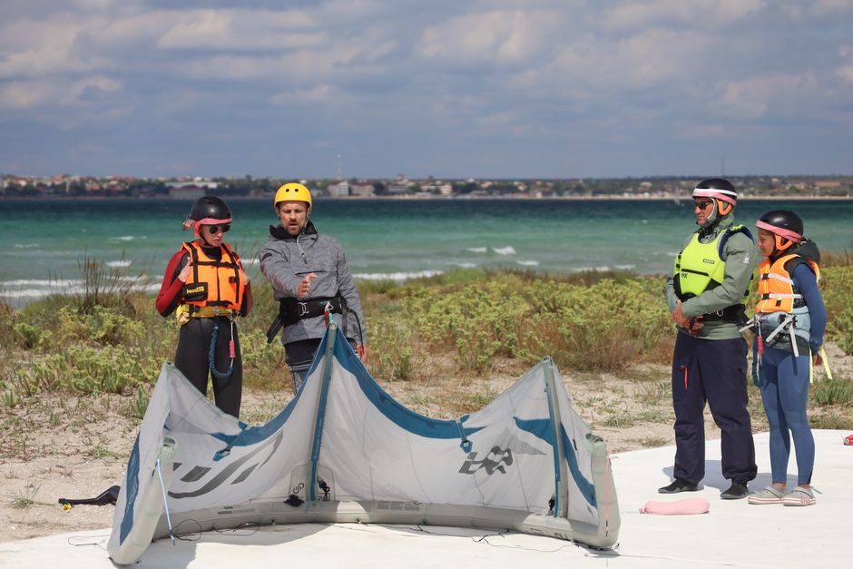 Instructors and students gathered around a kite on a beach