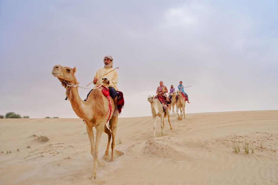Riders on camels crossing pale sand dunes