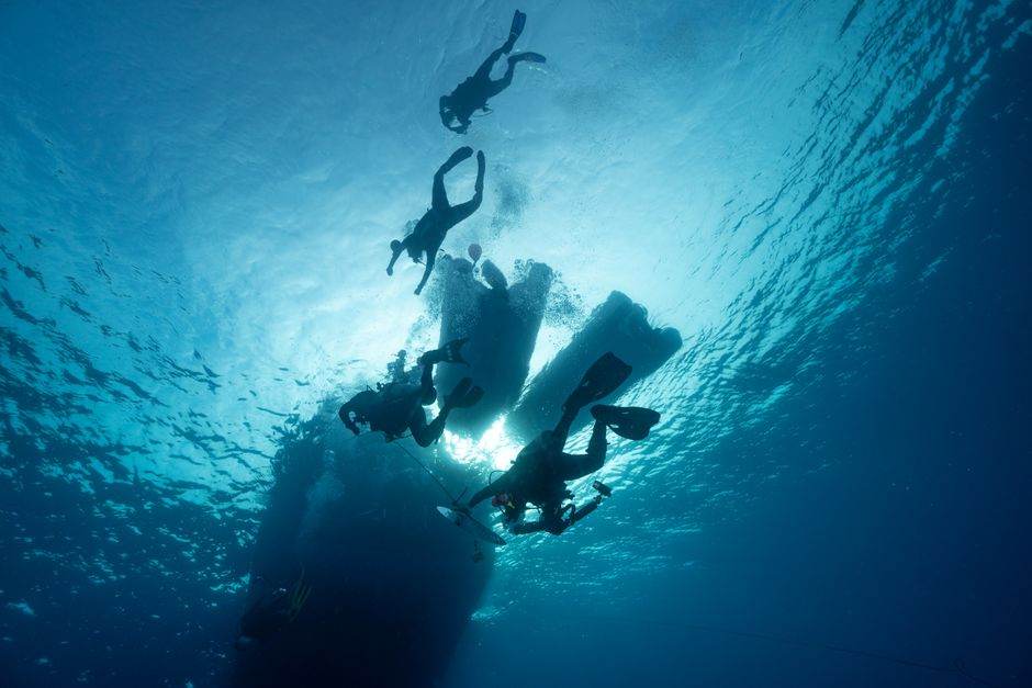 Divers descending in deep blue water lit from above