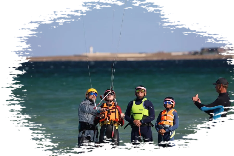 Kitesurf instructor and students in wetsuits and life vests standing in shallow water