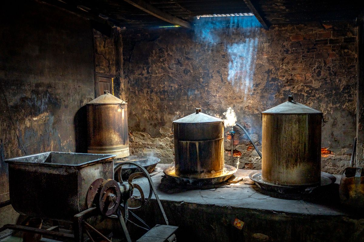 Old copper stills in a rustic distillery with light streaming through the roof