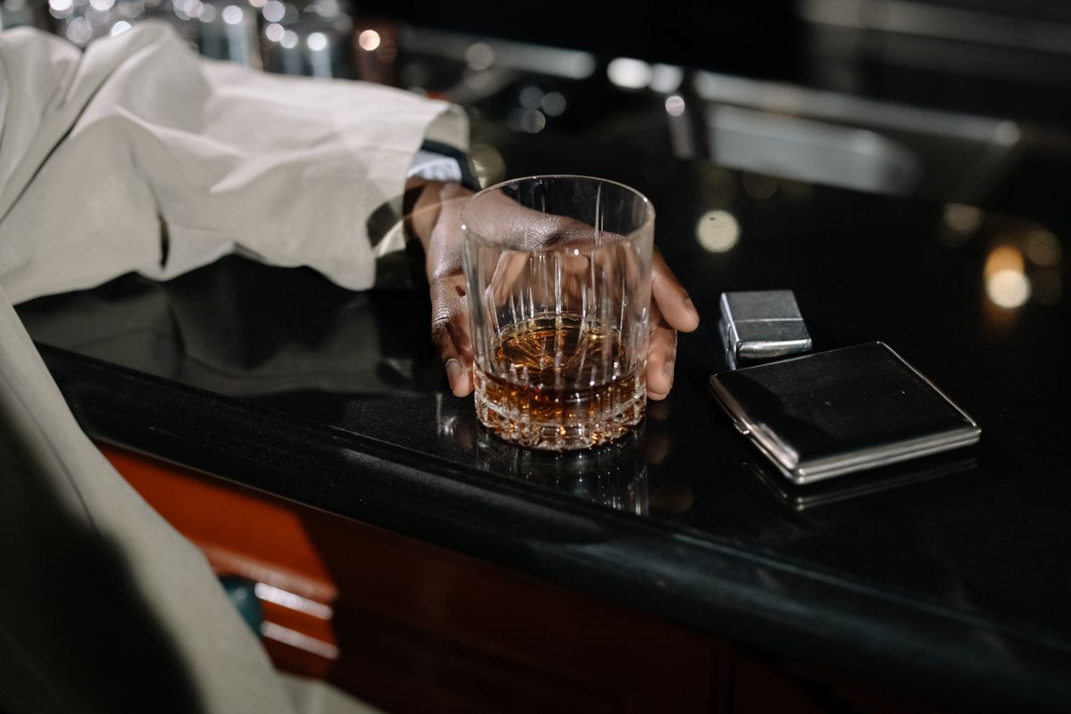 Hand resting on a cut-crystal glass of whisky on a dark bar