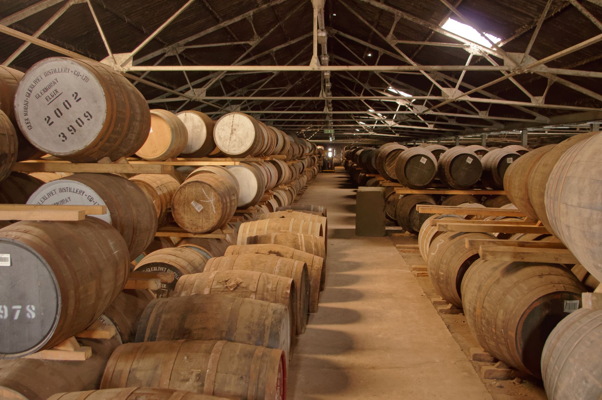 Rows of oak whisky barrels stacked on racks in a long warehouse