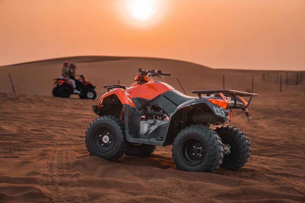 Orange quad bike parked on a dune at sunset