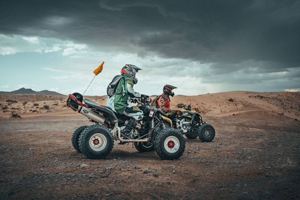 Two riders in helmets on quad bikes under a stormy sky