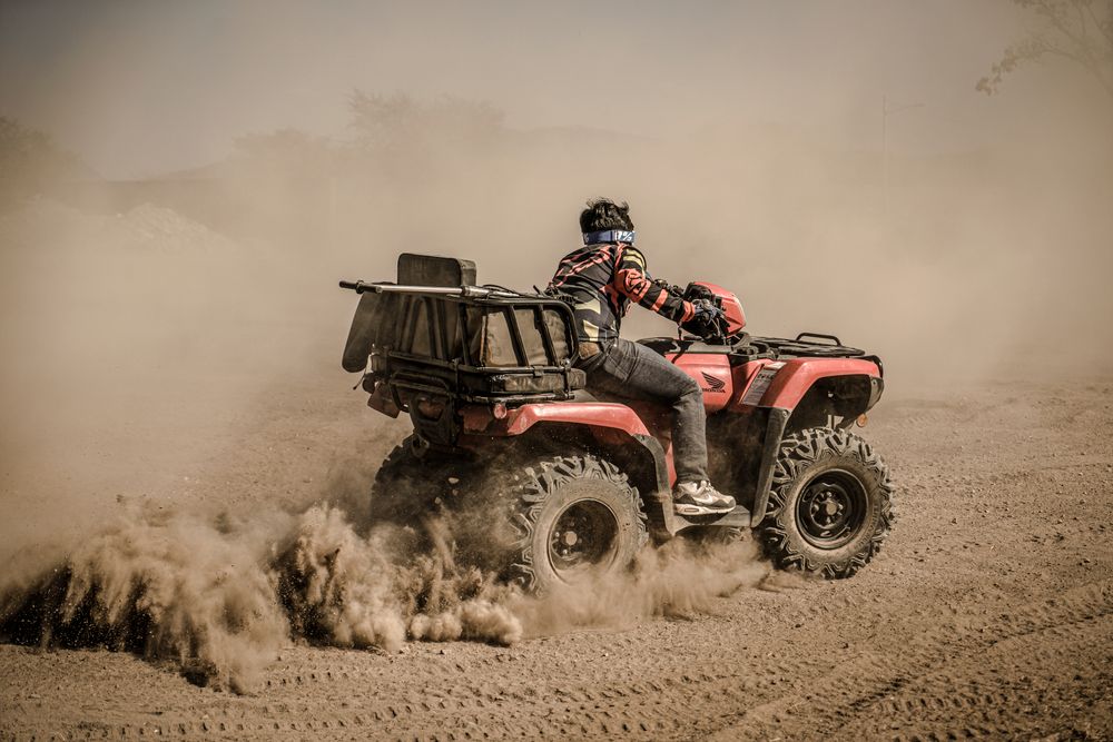 Rider on a red quad bike kicking up dust on a dirt track