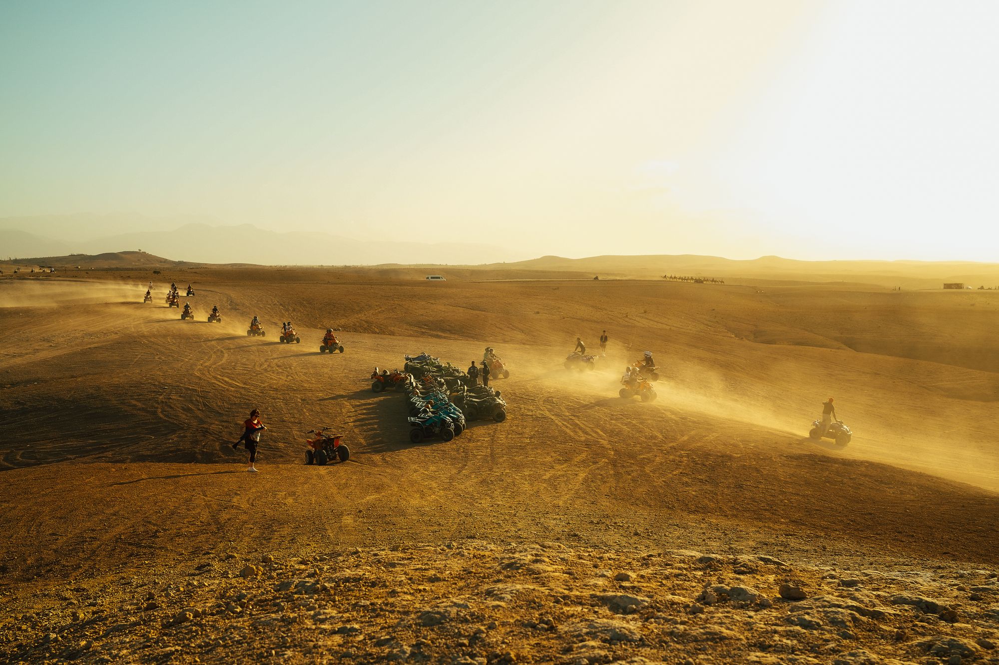 Line of riders on quad bikes crossing golden dunes in the evening light