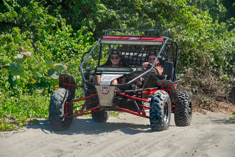 Two people driving a red off-road buggy along a sandy forest trail