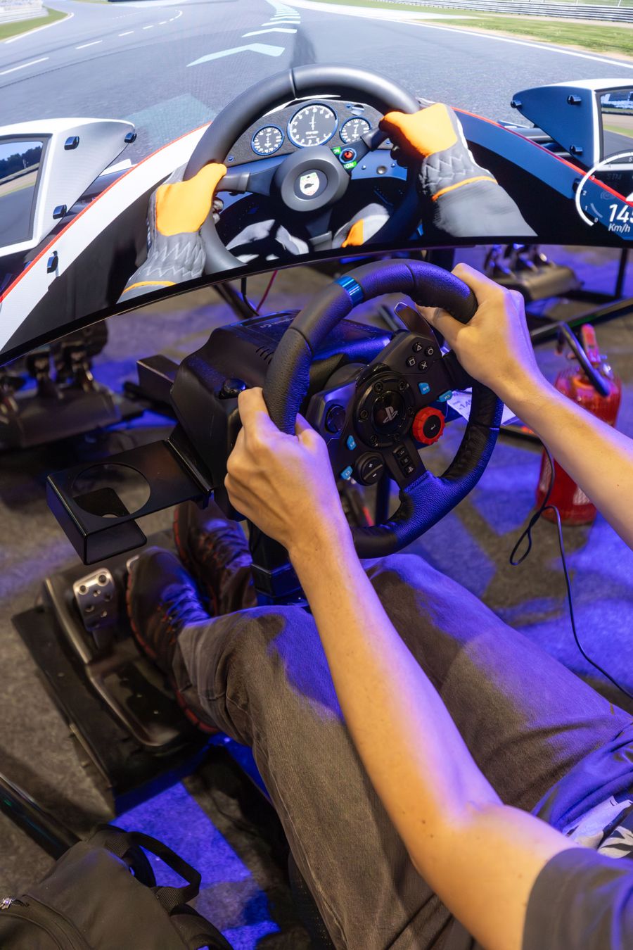Hands on a racing wheel inside a simulator with purple lighting