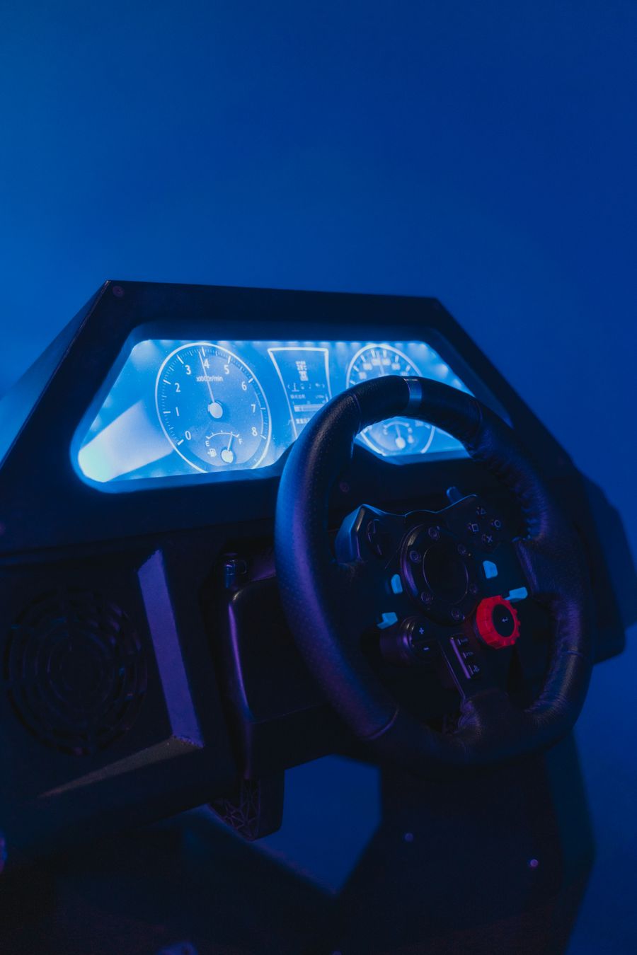Racing simulator cockpit lit in blue with a steering wheel and digital dashboard